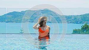 Woman in swimsuit enjoys stunning sea view from infinity pool