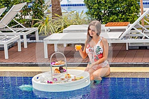 Woman in swimsuit with floating breakfast in swimming pool in luxury hotel