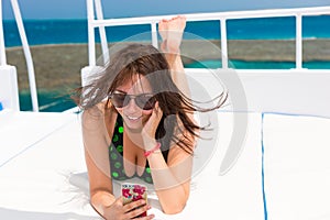 Woman in swimsuit lying on the deck of the yacht and takes a selfie at a sunny summer day