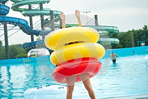 A woman in a swimsuit with rubber inflatable circles plays and has a good time near the pool of the summer water park