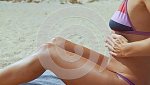 Woman in the swimsuit rubs into the skin tanning agent sitting on the sea beach