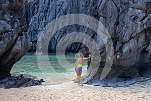 Woman in swimsuit on white sand beach with black rocks. Tropical seaside landscape. Black rock and white sand