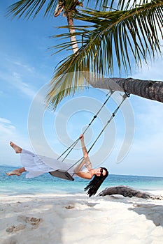 Woman on the swing on the beach in white dress