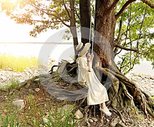 Woman on  swing on sea beach , large tree seascape  lady in straw hat  white dress on wild field watching to sea and sky panorama