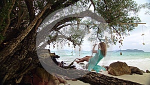 Woman swinging on a swing on a tropical beach, on shores of the turquoise sea