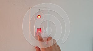 Woman switching off red button light on white wall