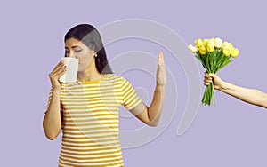 Woman with symptoms of allergic rhinitis refuses bouquet of flowers on pastel purple background.