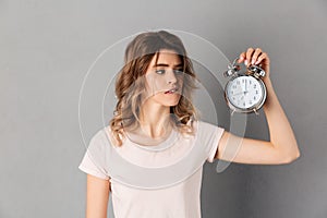 Woman in t-shirt bites lip and looking on alarm clock