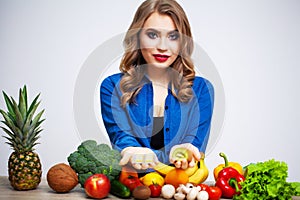 Woman at a table holding a kiwi and pills on a background of fruit and vegetables