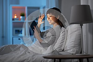 woman with tablet pc in bed has video call at night