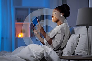 woman with tablet pc and earphones in bed at night