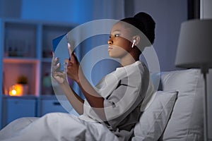 woman with tablet pc and earphones in bed at night