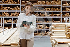 Woman with tablet in a timber and lumber warehouse. Product acceptance and quality control