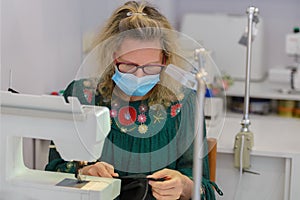 Woman tailor with a medical mask on her face works in a sewing atelier, work during quarantine