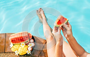 Woman take in hands little watermelon piece, sitting on the pool edge and enjoing fresh fruits