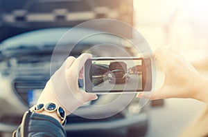 Woman take a photo. Broken car on a background. Woman sit on a wheel.woman repair a car. Natural background. Car accide