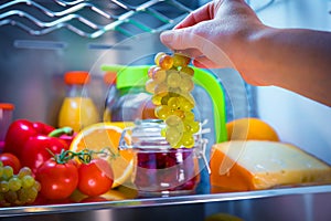 Woman takes the bunch of grapes from the open refrigerator