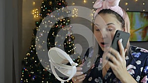 A woman takes care of her beautiful skin on her face, standing near the Christmas tree. Young woman applying foundation