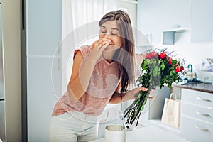 Woman takes dead roses out of vase feeling bad smell. Housewife taking care of coziness on kitchen photo