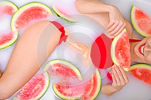 A woman takes a milk bath with slices of watermelons. SPA skin care treatments. Girl in a red bikini. Red lipstick