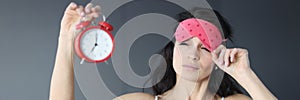 Woman takes off her sleep mask and looks at alarm clock