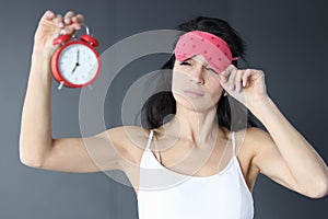 Woman takes off her sleep mask and looks at alarm clock