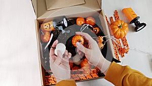 a woman takes out small pumpkins from a box with halloween decorations