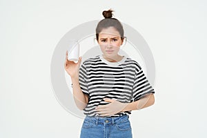 Woman takes painkillers, pills from stomach ache, menstrual pain, holds hand on belly, shows bottle with tablets, stands