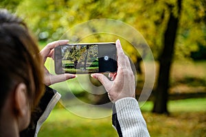A woman takes a photo of a beautiful autumn landscape using her phone
