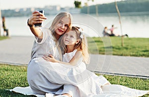 Woman takes photo of herself and daughter. Photo of young mother and her daughter having good time on the green grass