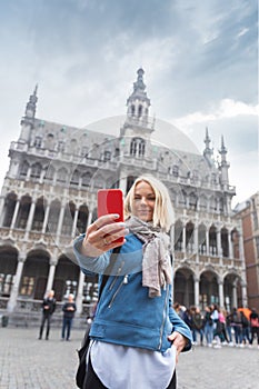 A woman takes pictures on her phone against the backdrop of the Museum of the City of Brussels in the main square Grand