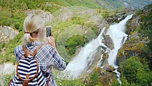 Woman takes pictures of a picturesque waterfall in Norway. Briksdal glacier