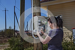 Woman takes readings of the electric meter, outdoors.