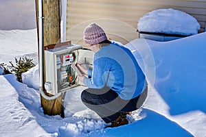 Woman takes readings from external electric meter outside in winter.