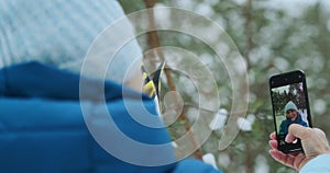 A woman takes a selfie using her phone, poses for the camera in a winter forest