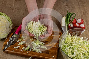 The woman takes shredded white cabbage with her hands and puts the cabbage in a bowl of salad. A housewife prepares a