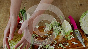 The woman takes shredded white cabbage with her hands and puts the cabbage in a bowl of salad. A housewife prepares a