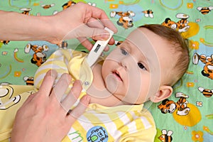 The woman takes temperature to the sick baby the electronic thermometer