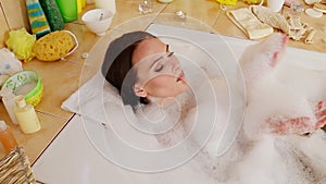 Woman taking bath and blowing on foam in her bathroom.