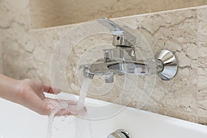 Woman taking a bath checking temperature touching running water with hand