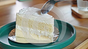 Woman taking a bite of coconut cake with fork. It is a cake frosted with a white frosting and covered with pieces of fresh coconut