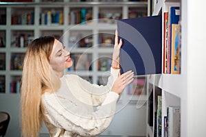 Woman taking book from library bookshelf. Young librarian searching books and taking one book from library bookshelf.