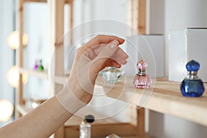 Woman taking bottle of perfume from wooden shelf, closeup