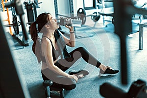 Woman taking a break and  drinking water after workout at gym