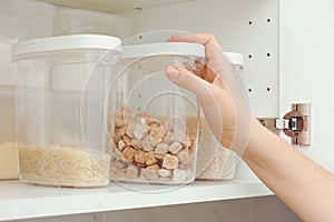 Woman taking brown cane sugar from a kitchen cupboard