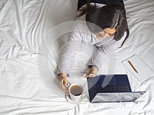 Woman taking a call in pijama in bed drinking coffee in the morning. photo