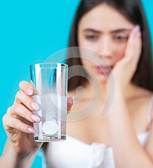 Woman taking drugs to releave headache. Brunette take some pills, holds glass of water, isolated on blue. Young woman