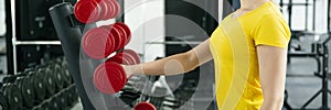 Woman taking dumbbells in the fitness gym with dumbbells on rack