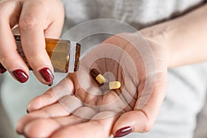 Woman taking gastritis, stomach ulcer, heartburn medicine capsule pouring pills from meds bottle in female hand