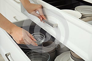 Woman taking glass bowl from open drawer of kitchen cabinet, closeup